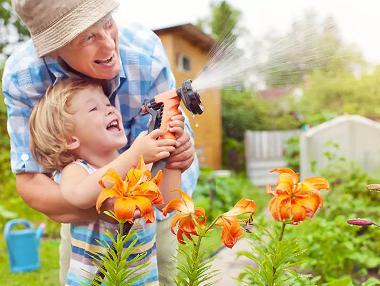 Man watering garden with grandchild