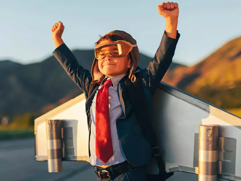 Child in business suit with jet plan wings imagining flight