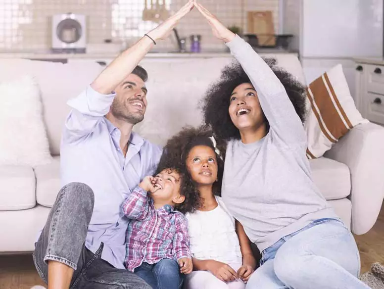 Family of four in living room making roof shape with hands